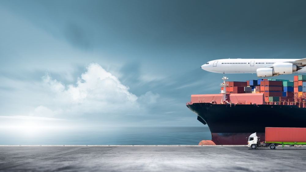 Airplane flying over cargo ship and truck at dock