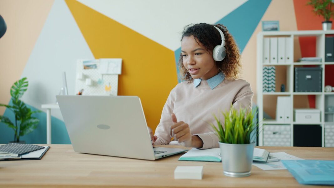 Woman wearing headphones works on a laptop at a desk.